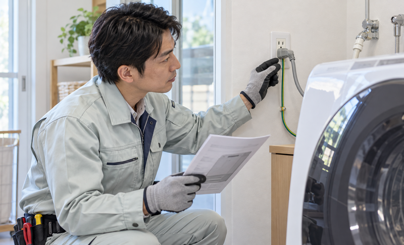洗濯乾燥機のコンセントとアース線を確認する電気工事士のイメージ